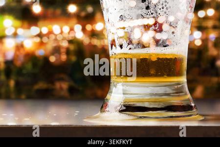 Nahaufnahme eines halb leeren Bierglases auf einem Tisch mit Schaum und Blasen, umgeben von warmen Bokeh-Lichtern in lebhafter Bar-Atmosphäre. Stockfoto