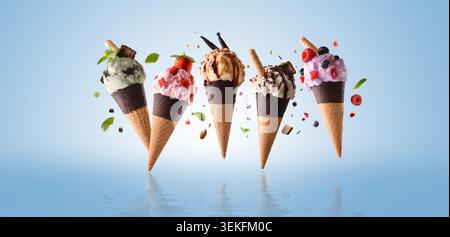 Fünf bunte Eiskegel mit verschiedenen Geschmacksrichtungen und Belägen, die über einer reflektierenden Oberfläche vor einem klaren blauen Hintergrund schweben. Stockfoto