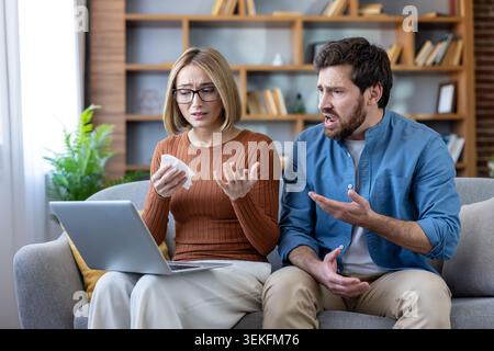 Beziehungsschwierigkeiten treten auf, während ein junges Paar zu Hause auf einem Sofa sitzt, während die Frau weint und ein Taschentuch hält, während sie einen Laptop A ansieht Stockfoto