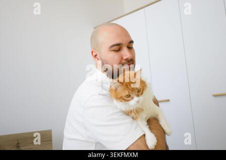 Glücklicher Mann, der ein flauschiges Katzentier hält und zu Hause Spaß hat Stockfoto