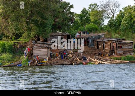 Menschen, die täglich Aktivitäten rund um eine lebendige afrikanische Siedlung am Fluss Unternehmen, mit rustikalen Holzhütten und vielen farbenfrohen traditionellen Kanus Stockfoto
