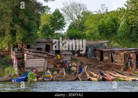 Menschen, die täglich Aktivitäten rund um eine lebendige afrikanische Siedlung am Fluss Unternehmen, mit rustikalen Holzhütten und vielen farbenfrohen traditionellen Kanus Stockfoto