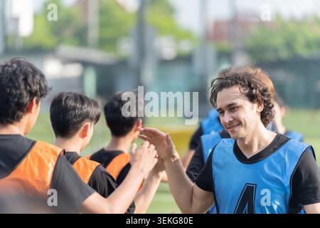 Kaukasische männliche Fußballspieler High Fives Teamkollegen auf einem Freifeld vor oder nach einem Spiel und zeigen Fairplay, Teamwork, Ermutigung und Stockfoto