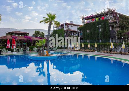 Hotel-Schwimmbecken umgeben von Palmen, efeubewachsenen Gebäuden und tropischer Gartenlandschaft an einem sonnigen Sommertag Stockfoto
