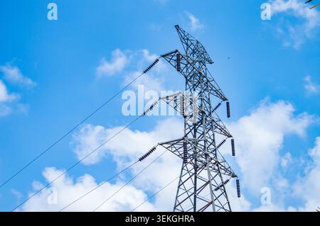 Eine Niedrigwinkelaufnahme eines Hochspannungs-Stahlgitterturms, der Stromleitungen gegen einen hellblauen Himmel mit verstreuten weißen Wolken trägt Stockfoto