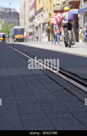 Stadtstraße mit einer Straßenbahnlinie im Vordergrund, die den städtischen Nahverkehr und die Fußgängeraktivitäten mit einem defokussierten Hintergrund erfasst und die tägliche Nutzung veranschaulicht Stockfoto