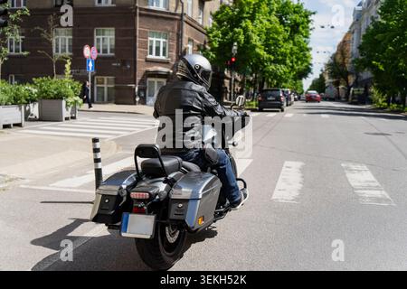 Ein Motorradfahrer mit Helm und Lederjacke auf einem Cruiser-Motorrad, der an einer Kreuzung wartet, individuelle städtische Verkehrsmittel und moderne persönliche M Stockfoto