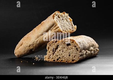 Nahaufnahme eines frisch gebackenen Sauerteigbrotlades, der auf dunkler Oberfläche in zwei Stücke gebrochen ist Stockfoto