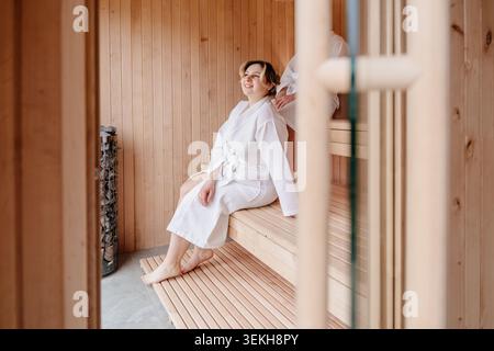 Lächelnde Junge Weiße Frau, Die Sich In Der Holzsauna Mit Partner Entspannt Stockfoto
