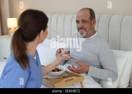 Die Pflegekraft frühstückt einem älteren Mann zu Hause im Bett Stockfoto