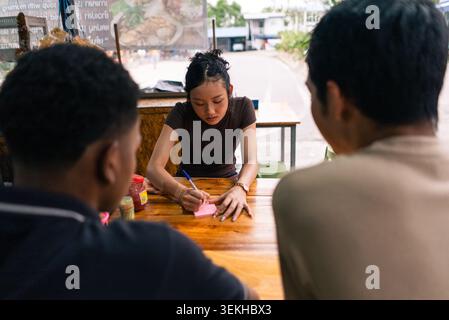 Eine junge asiatische Frau, die Bestellungen von Kunden an einem Verkaufsstand im Freien entgegennimmt Stockfoto
