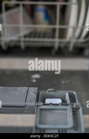 Spülmittelfach Für Geschirrspüler Mit Geöffneter Dosierschublade In Der Unteren Tür Senkrecht Mit Tablette Im Spender Und Verschwommenem Geladenem Rack Im Hintergrund Des Kücheninnenraums. Stockfoto