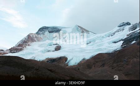 Die Nahaufnahme eines schneebedeckten Berges zeigt eindrucksvolle Kontraste mit braunem Gelände, mit einem markanten Gletscher vor der Kulisse des klaren Himmels Stockfoto