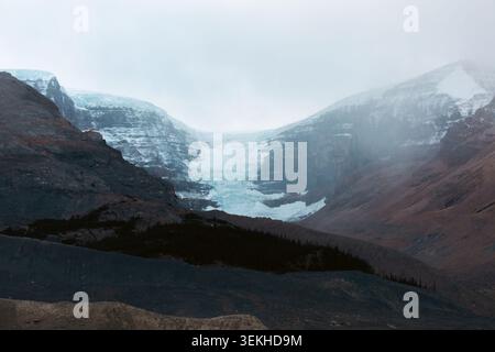 Die Nahaufnahme eines schneebedeckten Berges zeigt eindrucksvolle Kontraste mit braunem Gelände, mit einem markanten Gletscher vor der Kulisse des klaren Himmels Stockfoto