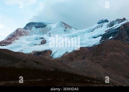 Die Nahaufnahme eines schneebedeckten Berges zeigt eindrucksvolle Kontraste mit braunem Gelände, mit einem markanten Gletscher vor der Kulisse des klaren Himmels Stockfoto