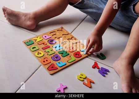 Nahaufnahme einer Hand eines Kleinkindes, die den blauen Holzbuchstaben „Z“ in den passenden Schlitz auf einem Puzzletafel platziert. Frühlernkonzept. Stockfoto