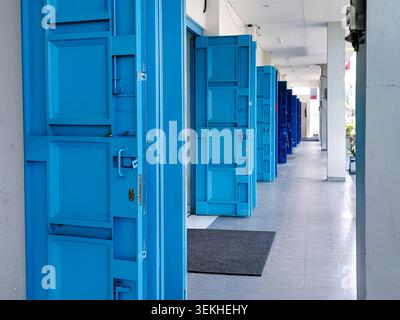 Eine klare perspektivische Aufnahme eines langen Flurs, der mit hellblauen Falttüren aus Metall gesäumt ist, zeigt sich wiederholende Muster, urbane Architektur und ein Gefühl für Tiefe in einem kommerziellen Ambiente. Stockfoto