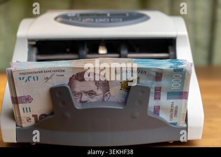 Nahaufnahme eines automatischen Bargeldzählautomaten, beladen mit einem Stapel von 1000 ukrainischen Griwna-Banknoten. Finanz- und Bankkonzept, Währungsumtausch Stockfoto