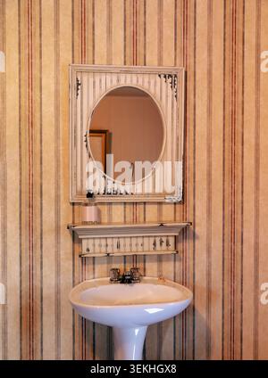 Altes Badezimmer mit Spiegel an der Tapetenwand mit weißem Porzellanwaschbecken Stockfoto