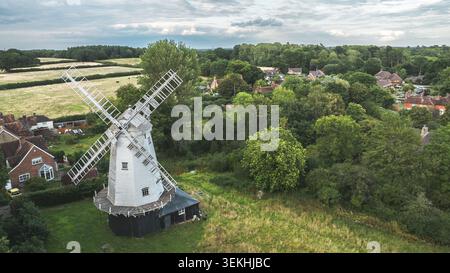 Aus der Vogelperspektive ist eine malerische ländliche Landschaft mit einer alten Windmühle umgeben von Bäumen, Feldern und charmanten Häusern Stockfoto