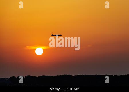 Passagierflugzeug fliegt über dem orangefarbenen Himmel bei Sonnenuntergang über der dunklen Silhouette Stockfoto