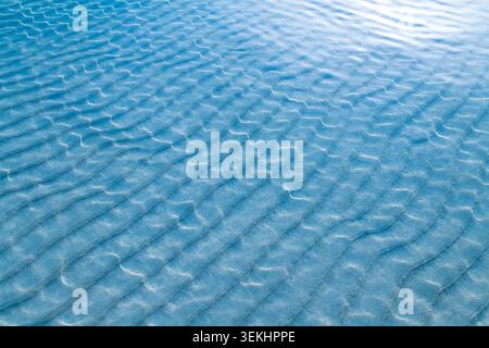 Strandsand kräuselt sich, Sonnenlicht und kristallklares Flachwasser. Stockfoto