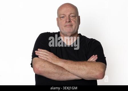 60 Jahre alter Schwarzer Mann mit gekreuzten Armen, der auf die Kamera isoliert auf weißem Hintergrund blickt Stockfoto