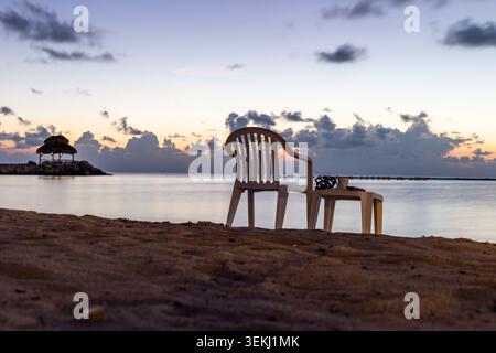 Blick auf einen Stuhl und eine Bank auf der Seite des Ozeans bei einem Sonnenaufgang Stockfoto