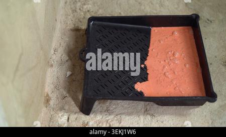 Schwarzes Farbtablett mit orangefarbener Farbe auf rauer Wand Stockfoto