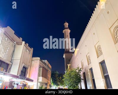 Blick auf die historische Straße mit einem Moschee-Minarett und traditionellen arabischen Gebäuden, die nach Sonnenuntergang beleuchtet werden Stockfoto