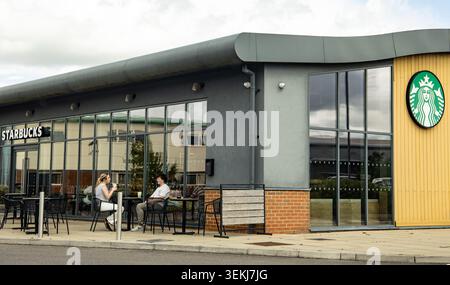 Junge Mann und Frau sprechen tagsüber an einem Tisch vor einem Starbucks-Café Stockfoto