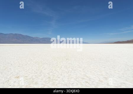 Badwater Basin Salzwasser im Death Valley Nationalpark erstrecken sich in strukturierten weißen Mustern zu fernen Wüstenbergen unter einem klaren blauen Himmel, s Stockfoto