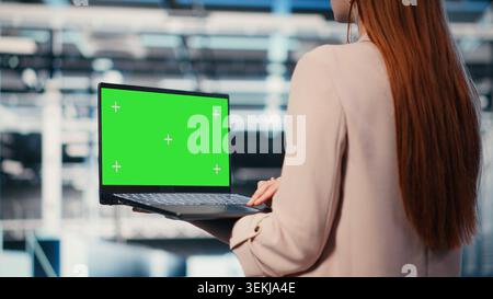 Green-Screen-Laptop, der von weiblichen Softwareentwicklern für Rechenzentren zur Verwaltung von Cloud-Computing-IT-Lösungen in Unternehmen mit Laptop verwendet wird. Frau, die ein Modell-Notebook benutzt, um die Serverfarm zu überwachen, Kamera B Stockfoto