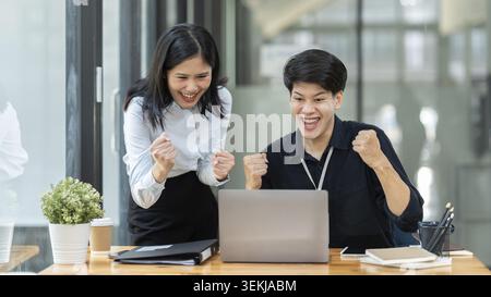 Geschäftskollegen, die sich ein Notebook ansehen und im Büro Erfolge feiern Stockfoto