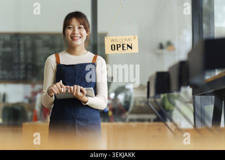Asiatischer Cafe-Besitzer oder Barista, der mit einem Lächeln im Café steht. Frau, Inhaber eines kleinen Unternehmens in der Gastronomie Stockfoto