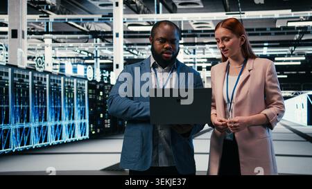Wartung, Laptop- und Engineering-Team im Server-Hub arbeiten zusammen, um Aufgaben zu erledigen. Konfiguration von Einstellungen, Servern und Teamkollegen im modernen High-Tech-Rechenzentrum, Kamera A Stockfoto