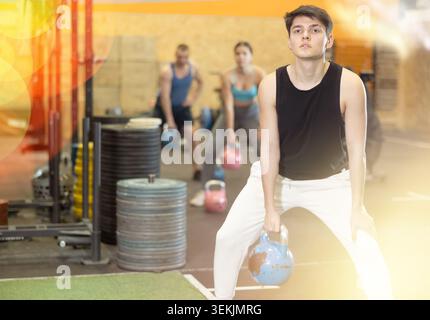 Motivierter Kerl, der Übungen mit Kettlebell im Fitnessstudio macht Stockfoto