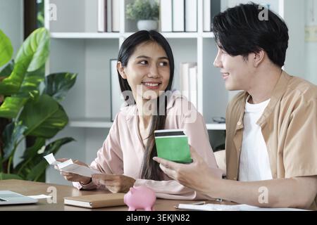 Ein junges Paar, das zu Hause über Finanzpläne diskutiert, umgeben von Dokumenten, Kreditkarten und einer Sparkasse in einem modernen Wohnzimmer Stockfoto