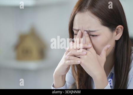 Eine Frau zeigt Anzeichen von emotionaler Belastung und hält ihr Gesicht frustriert, während sie an ihrem Schreibtisch sitzt. Erfasst Stress am Arbeitsplatz und psychische Gesundheit bewusst Stockfoto