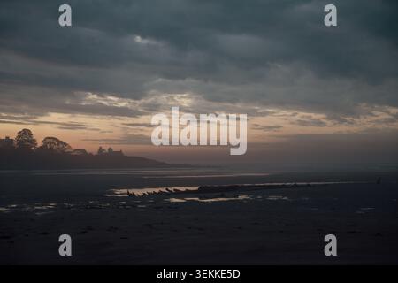 Blick auf den Strand auf ein Becken mit Wasser bei Ebbe bei einem bunten Sonnenaufgang mit Wolken am frühen Morgen Stockfoto