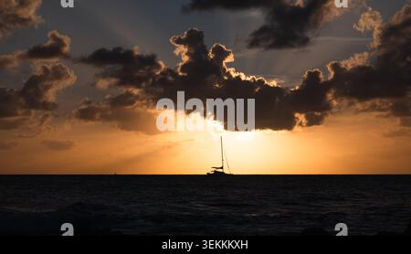 Felsiges Ufer mit Segelboot und spektakulärem Sonnenuntergang hinter dem Horizont Stockfoto