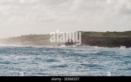 Blick auf eine Meeresküste mit den Wellen, die am Morgen unter dem Sonnenlicht gegen die hohen Felsen plätschern Stockfoto