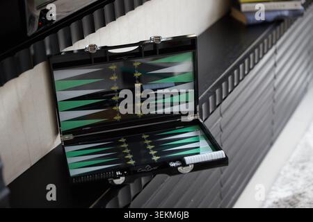 Offenes, luxuriöses Backgammon-Brett in Schwarz und Grün auf einem Innenregal mit Büchern und moderner Einrichtung im Hintergrund. Stockfoto
