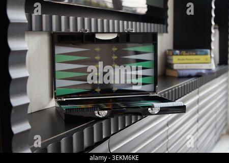 Offenes, luxuriöses Backgammon-Brett in Schwarz und Grün auf einem Innenregal mit Büchern und moderner Einrichtung im Hintergrund. Stockfoto