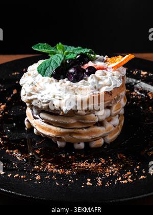 Zarte Pfannkuchen, hoch gestapelt mit Schlagsahne. Frische Beeren und Minze garnieren die Oberseite. Die Orangenschale sorgt für einen Farbakzent. Zerkrümelte Schokolade Stockfoto