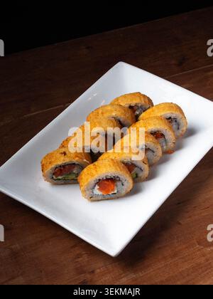 Goldbraune Brötchen ruhen auf einem weißen Teller. Frisches Gemüse blickt durch knusprigen Reis. Ein warmer Holztisch sorgt für rustikalen Charme. Perfekt für moderne japanische Cui Stockfoto