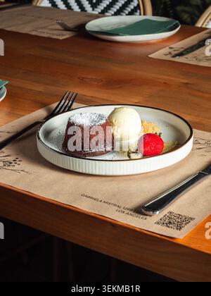 Ein warmer Holztisch bietet Platz für einen eleganten Dessertteller. Der Schokoladenkuchen sitzt neben einer Schaufel Vanilleeis. Frische Beerengarnitur sorgt für Farbe und Kondition Stockfoto