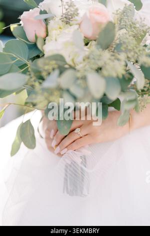 Intime Hochzeitsmomente mit Braut mit Blumen und Accessoires. Nahaufnahme einer Braut, die einen Blumenstrauß hält und ihren Ehering mit Eleganz zeigt Stockfoto