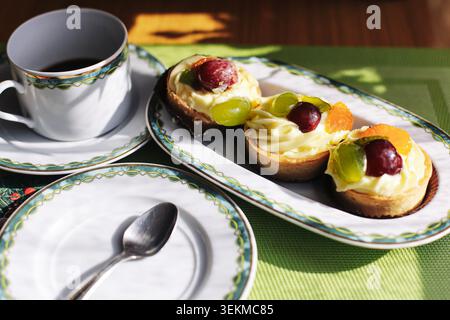 Obsttörtchen mit Sahne und Kaffee auf dem Tisch. Süßes Gebäck Frühstück und Dessert Konzept für Café oder Hausmannskost. Stockfoto