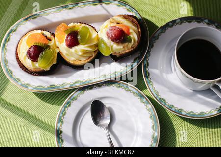 Kleine Obsttörtchen, serviert mit schwarzem Kaffee auf elegantem Geschirr. Dessert-Hintergrund für süße Gebäckstücke, Nachmittagssnack-Feier und Heimessen. Stockfoto